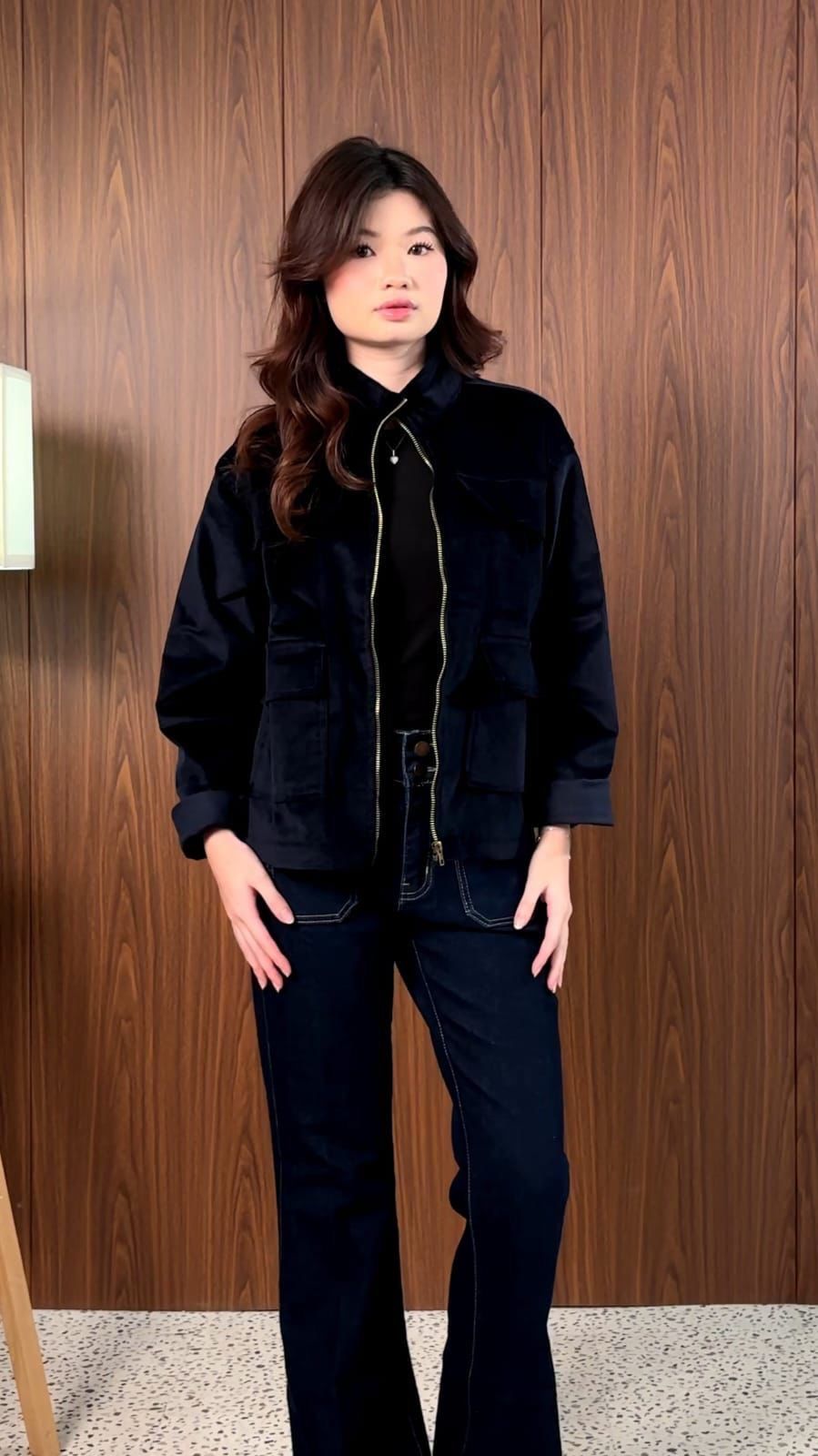 Navy longneck jacket with a brass zip, worn with dark flared jeans against a wood panel