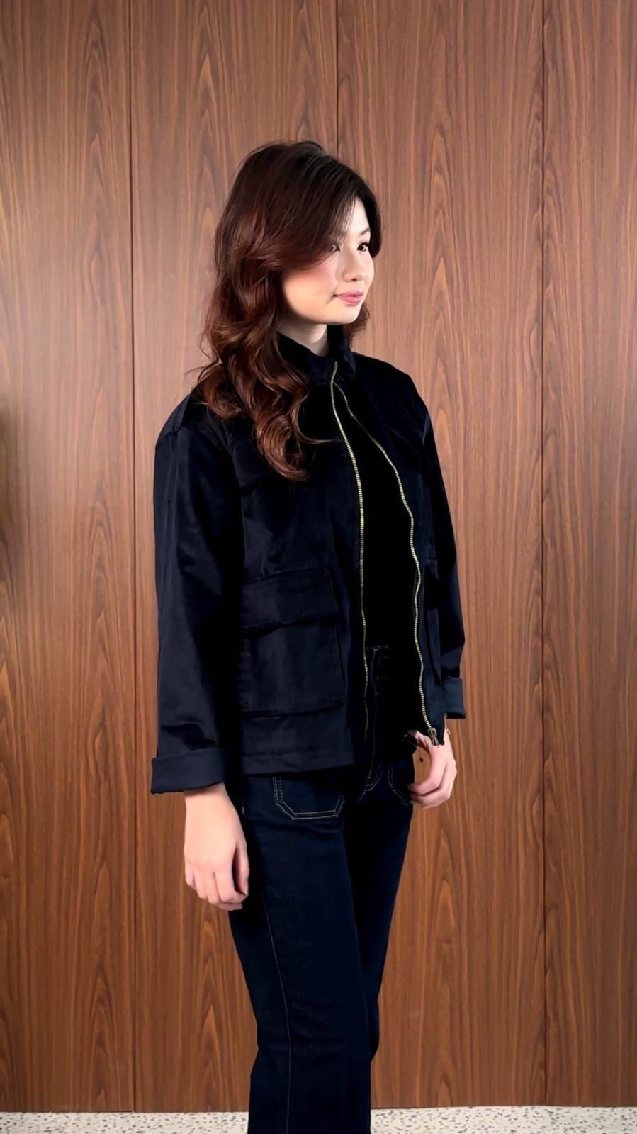 Navy longneck jacket with a brass zip, model glancing to the side against a wood panel