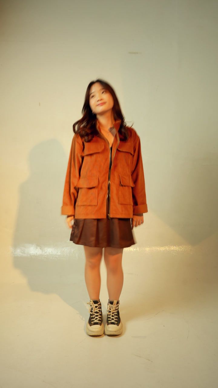 Model in the caramel longneck jacket standing still as people pass