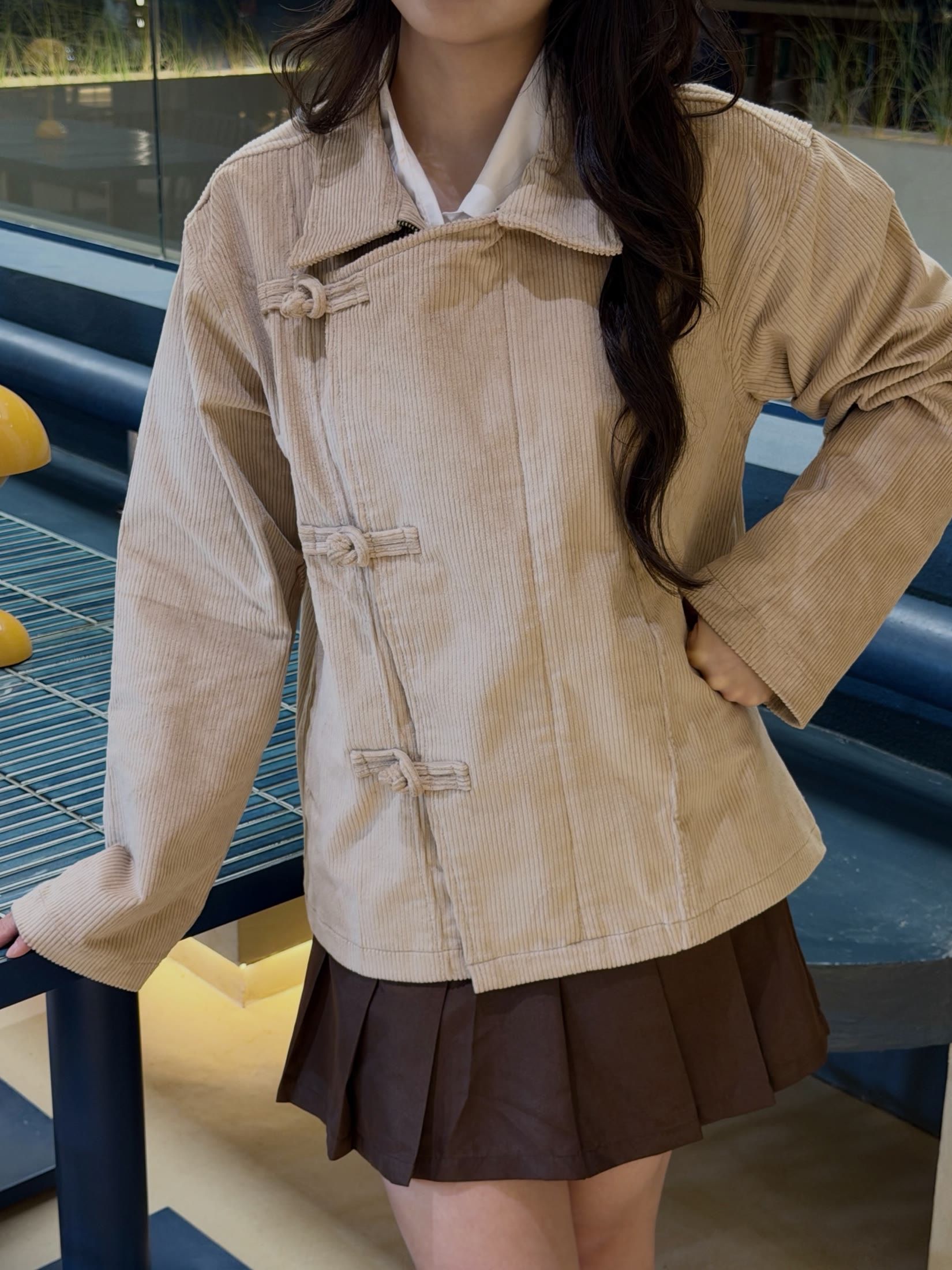 Close view of the cocoa pleated mini skirt worn with the cream cheongsam jacket
