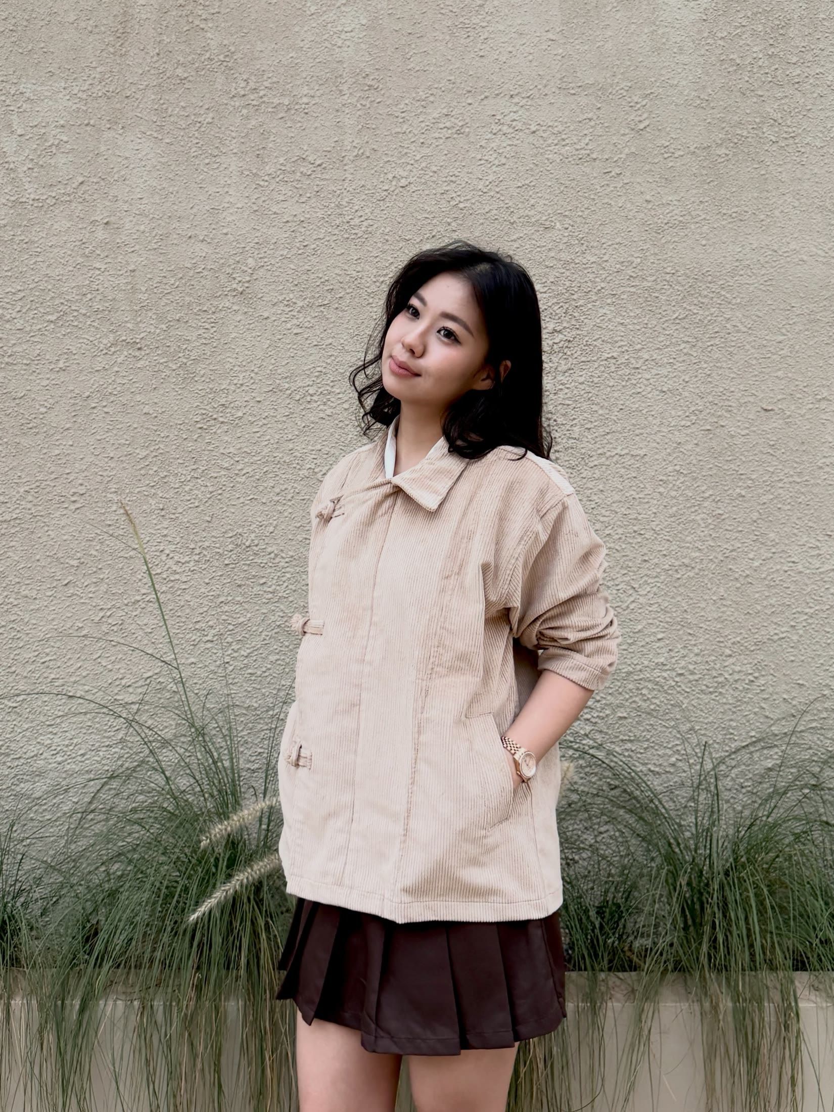 Cocoa pleated mini skirt, hand in the jacket pocket, by tall grass