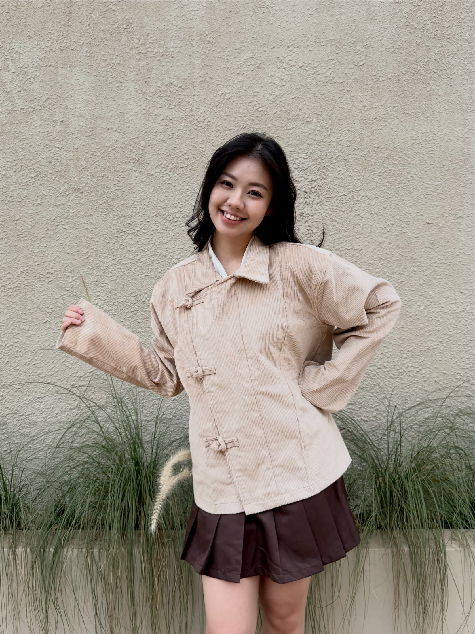 Model smiling in the cream cheongsam jacket and cocoa pleated skirt